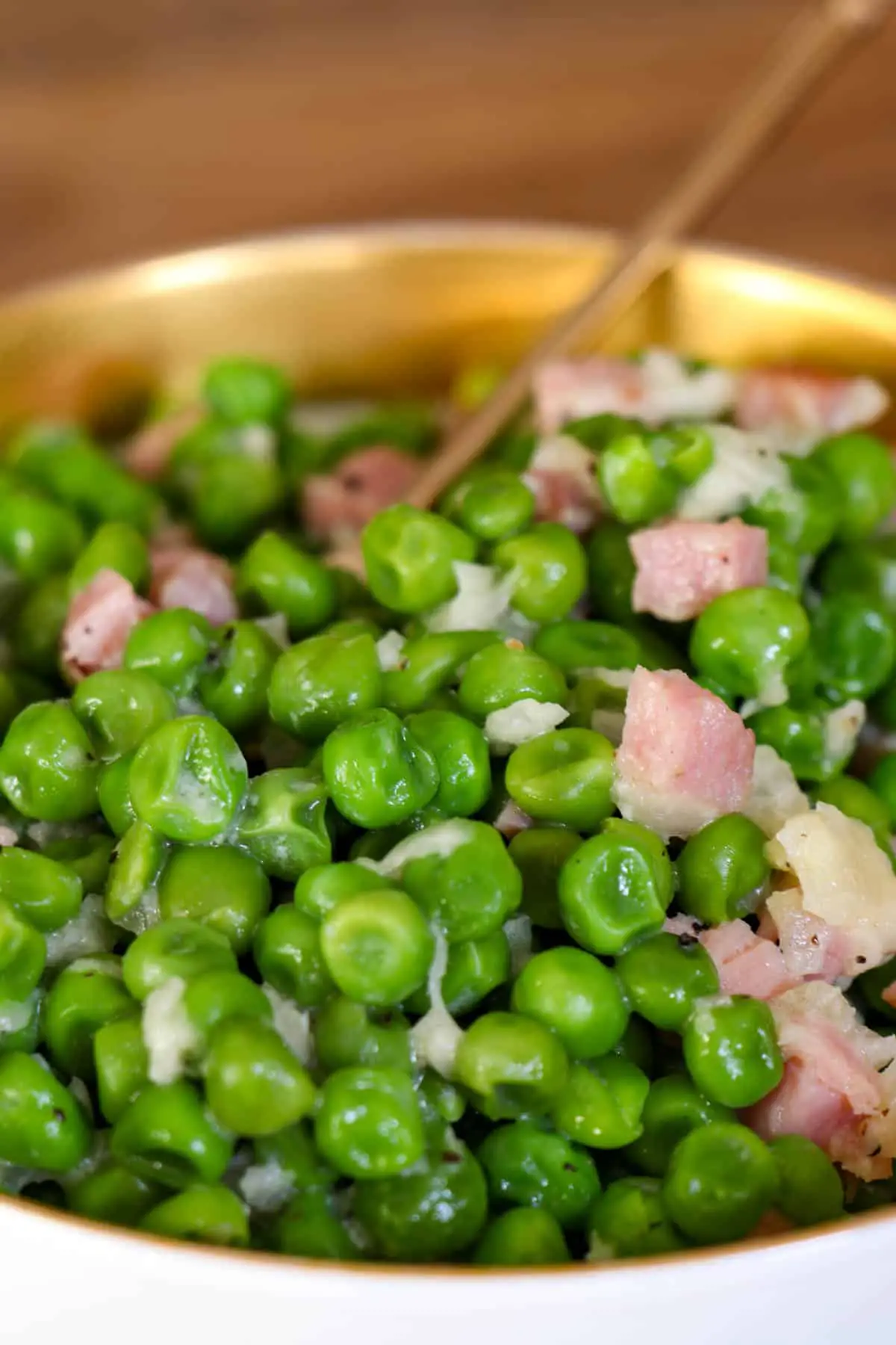 A gold rimmed bowl containing peas, ham, and onion with a gold stemmed spoon resting in the bowl.