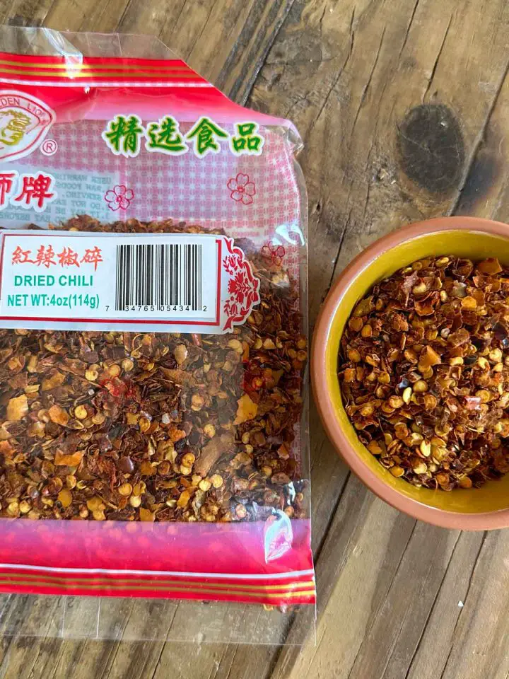A packet of dried Asian chili flakes and a small bowl containing some of those flakes.