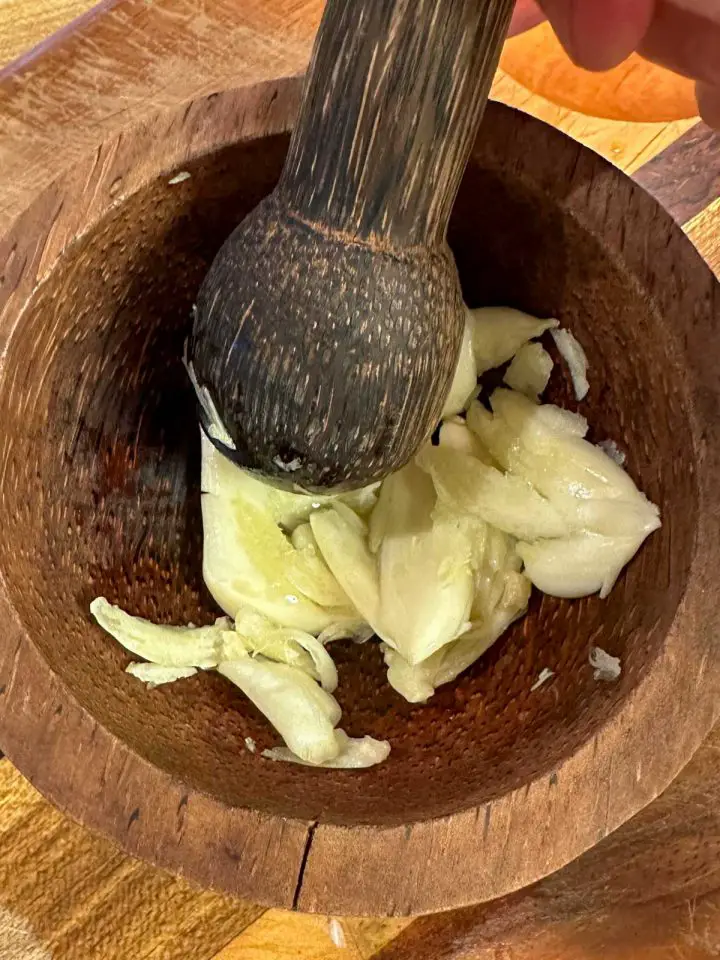 Crushed garlic in a mortar with a pestle on top of the garlic.