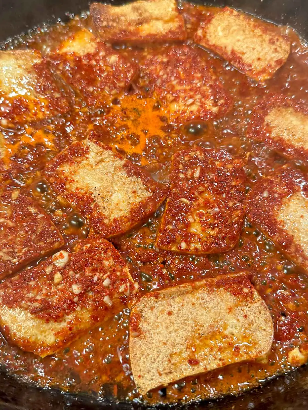 Pieces of browned tofu in a spicy simmering sauce in a cast iron skillet.