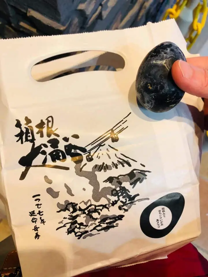 A shopping bag with a drawing of a volcano and a person holding a Hakone black egg.