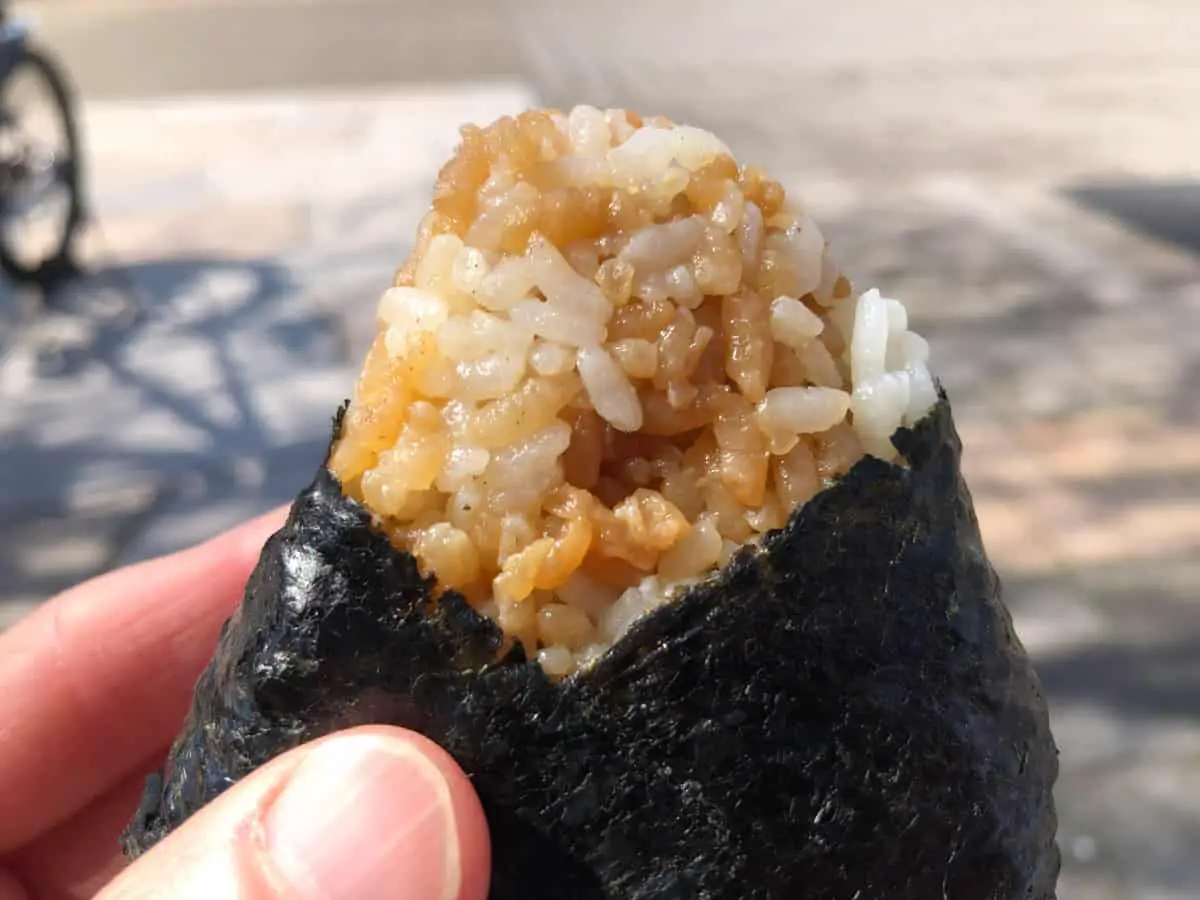 A hand holding onigiri which is a rice ball wrapped in seaweed. 