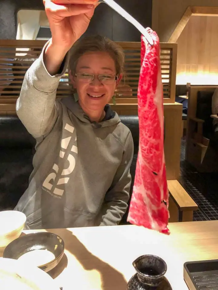 A woman holding a raw piece of meat with chopsticks.