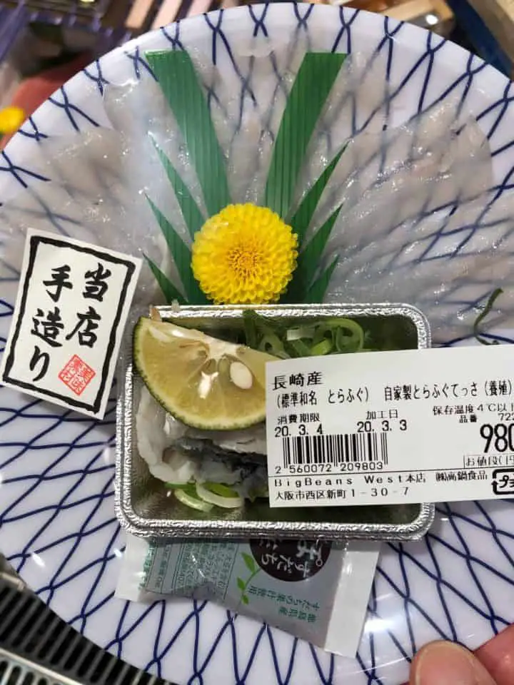 A small plate with sliced fugu and labels from the grocery store where it is being sold in Japan. There is also a chrysanthemum and leaves on the package.