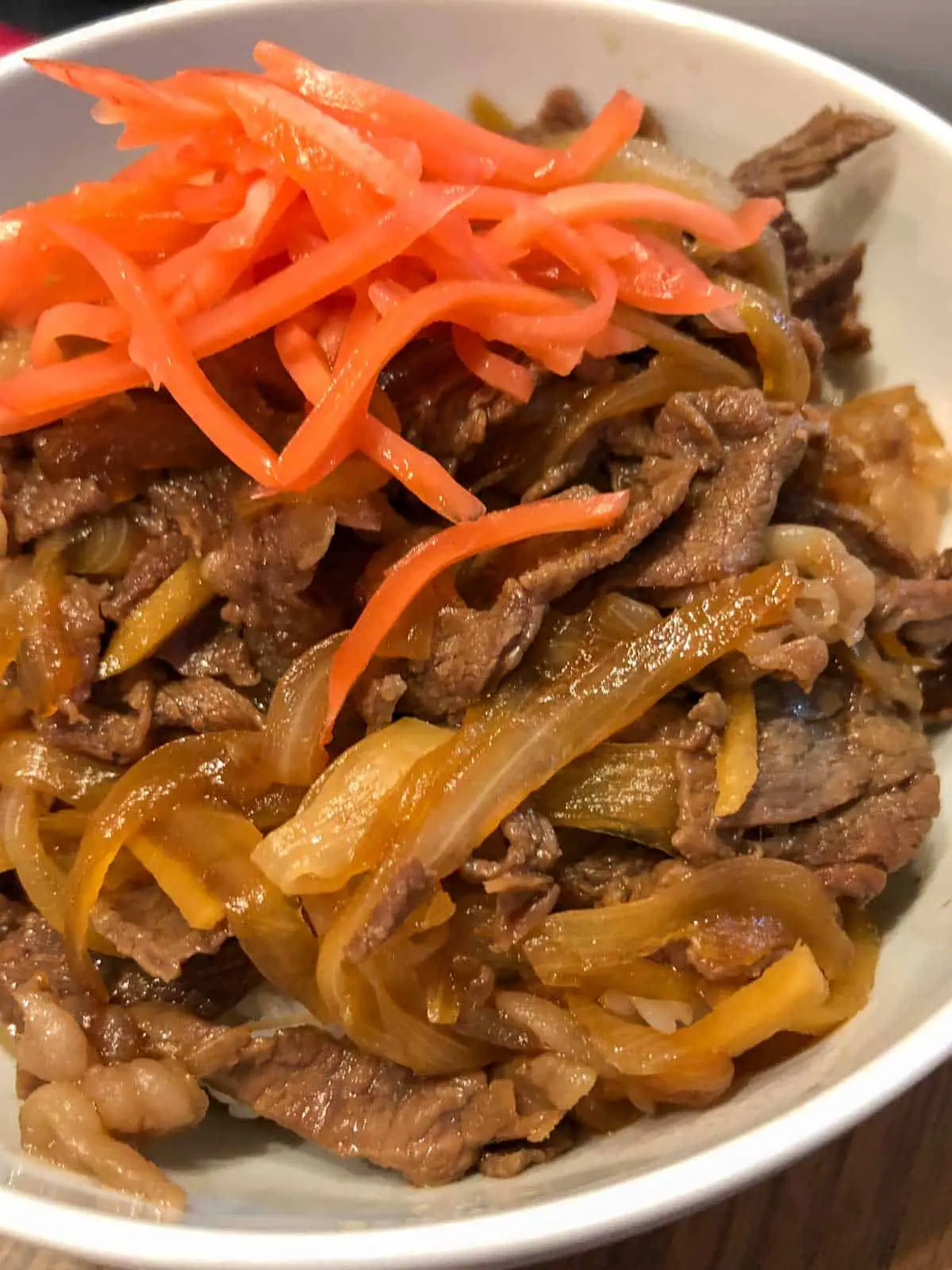 A white bowl with slices of beef and onion topped with pickled ginger. 