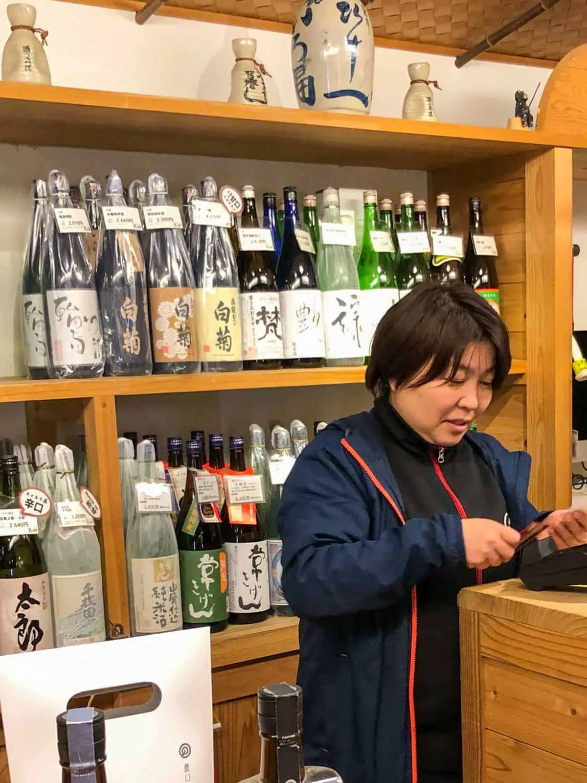 A woman in a shop that sells sake. There are many different bottles of sake on shelves in the shop.