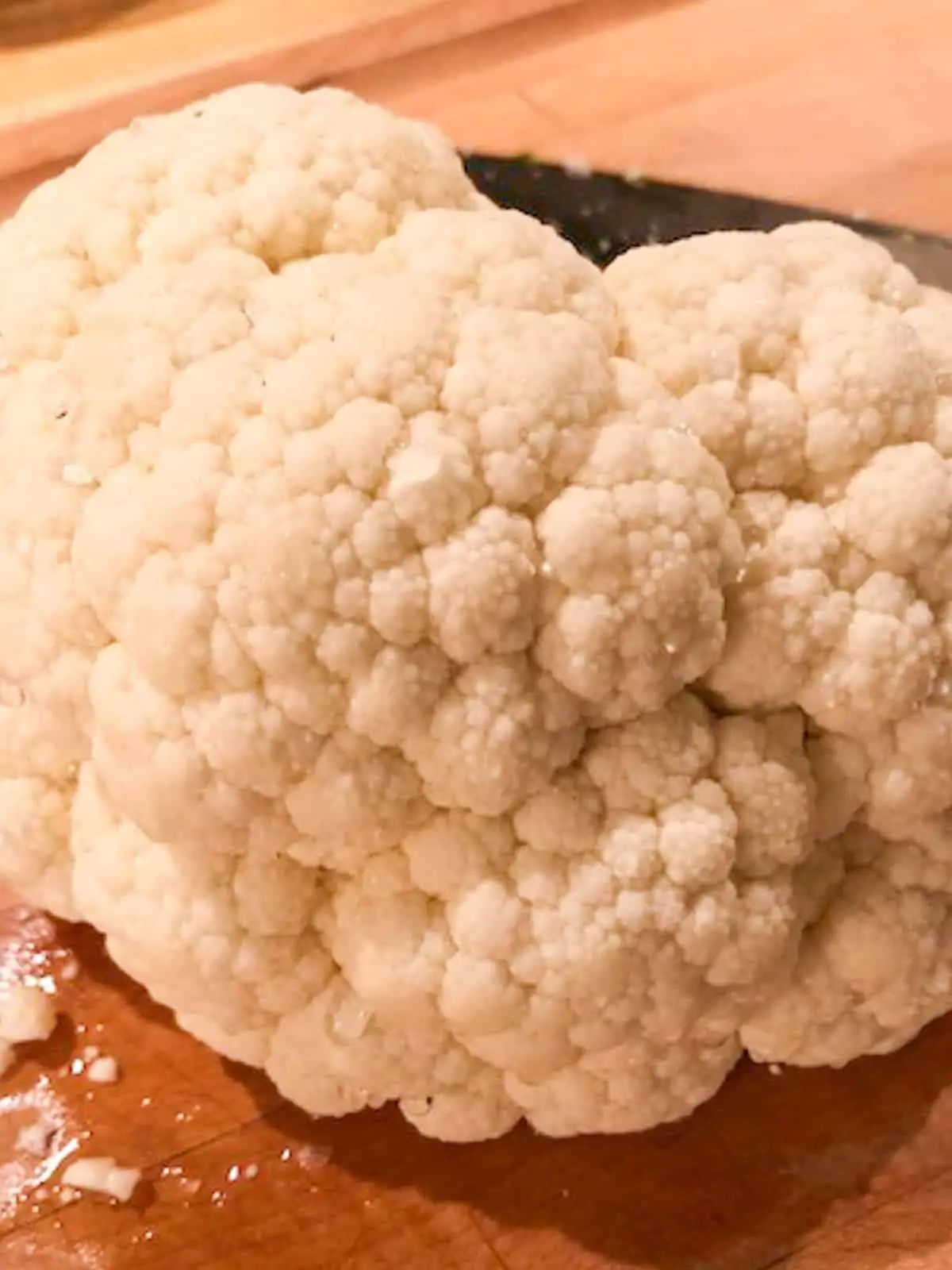 A close up of a head of cauliflower with a glimpse of a knife in the background.
