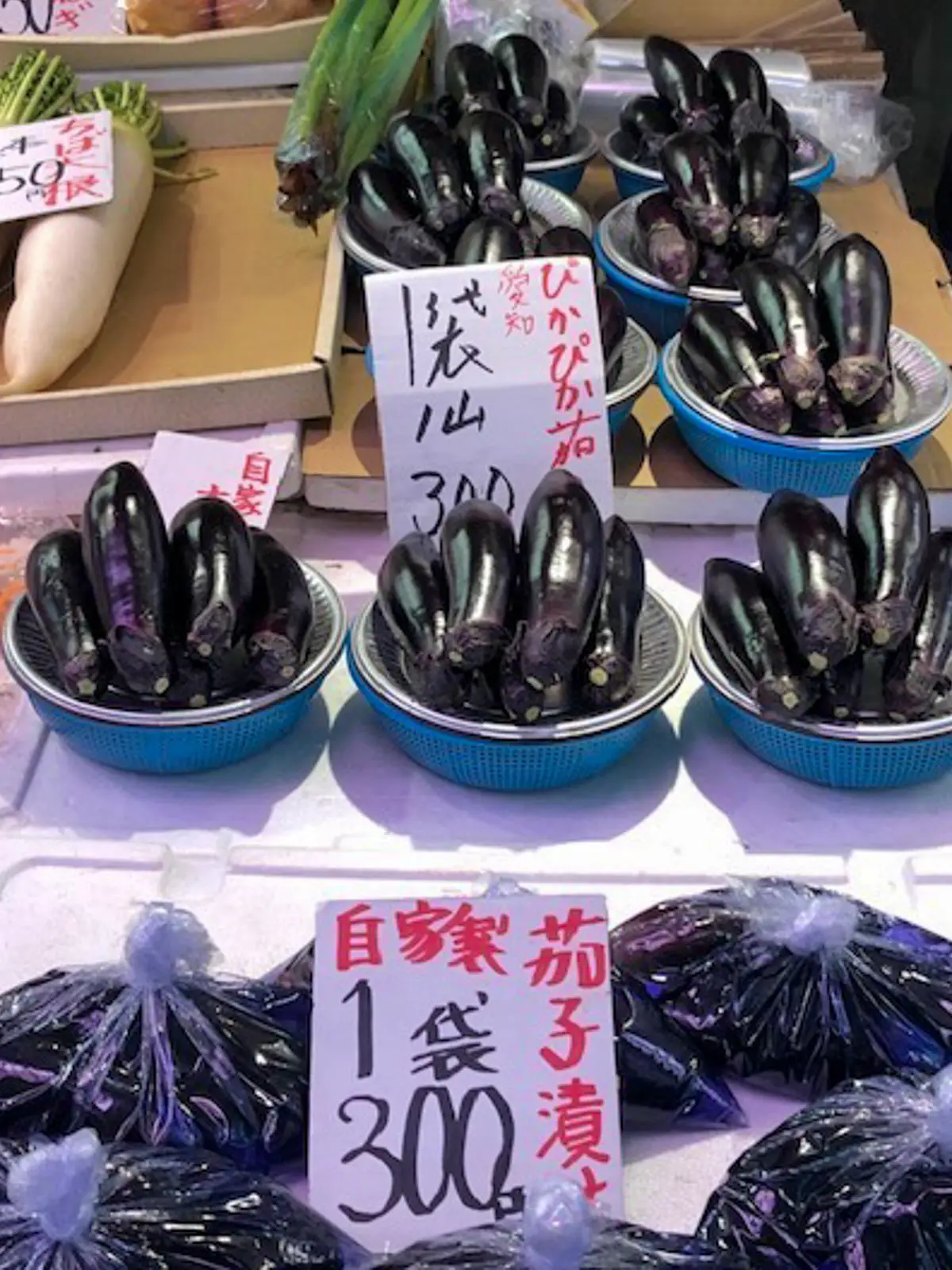 Several bowls filled with Japanese eggplants on display for sale in a market. 