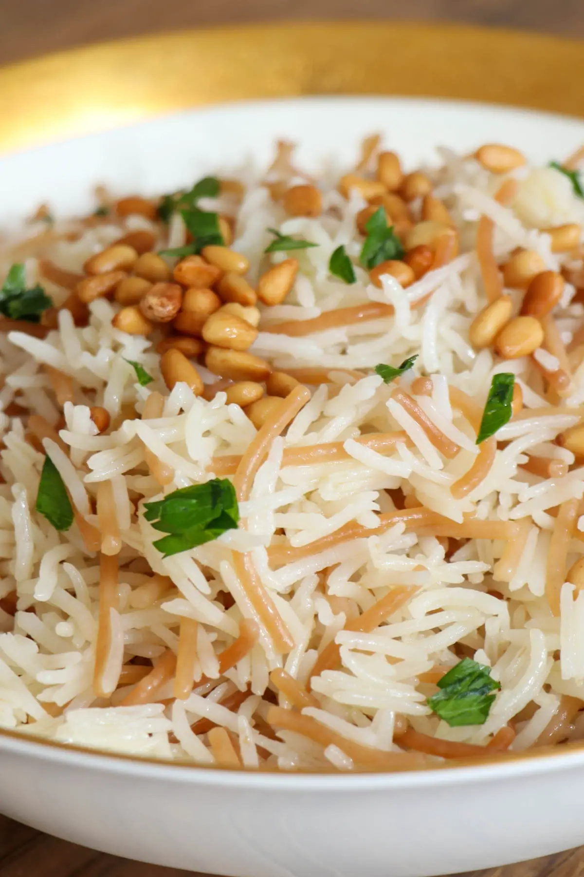 A gold rimmed bowl containing a combination of basmati rice and vermicelli topped with toasted pine nuts and minced Italian parsley.