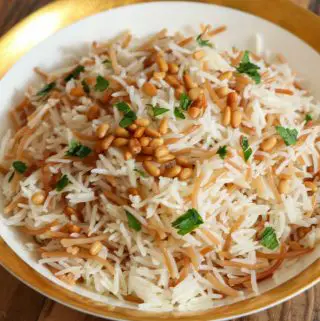 A gold rimmed bowl containing a combination of basmati rice and vermicelli topped with toasted pine nuts and minced Italian parsley.