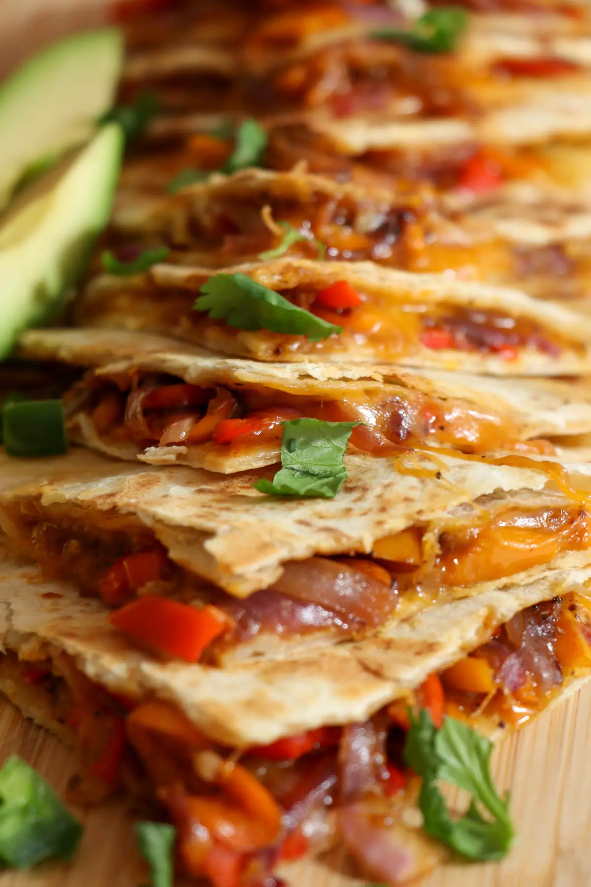 Quesadillas filled with melted cheese and sautéed vegetable mixture. There are slices of avocado and cilantro leaves garnishing the quesadilla wedges.