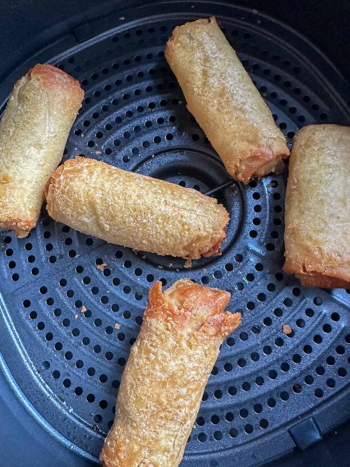 5 cooked egg rolls in an air fryer basket.