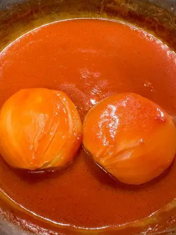 A saucepan containing tomato soup with 2 onion halves in the saucepan.