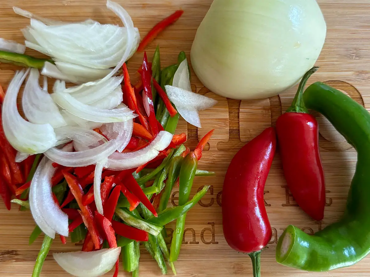 Sliced onion, and red and green peppers, next to half an onion, 2 red chilies and a green chili.