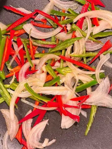 Slices of onion, red pepper, and green pepper in a wok.