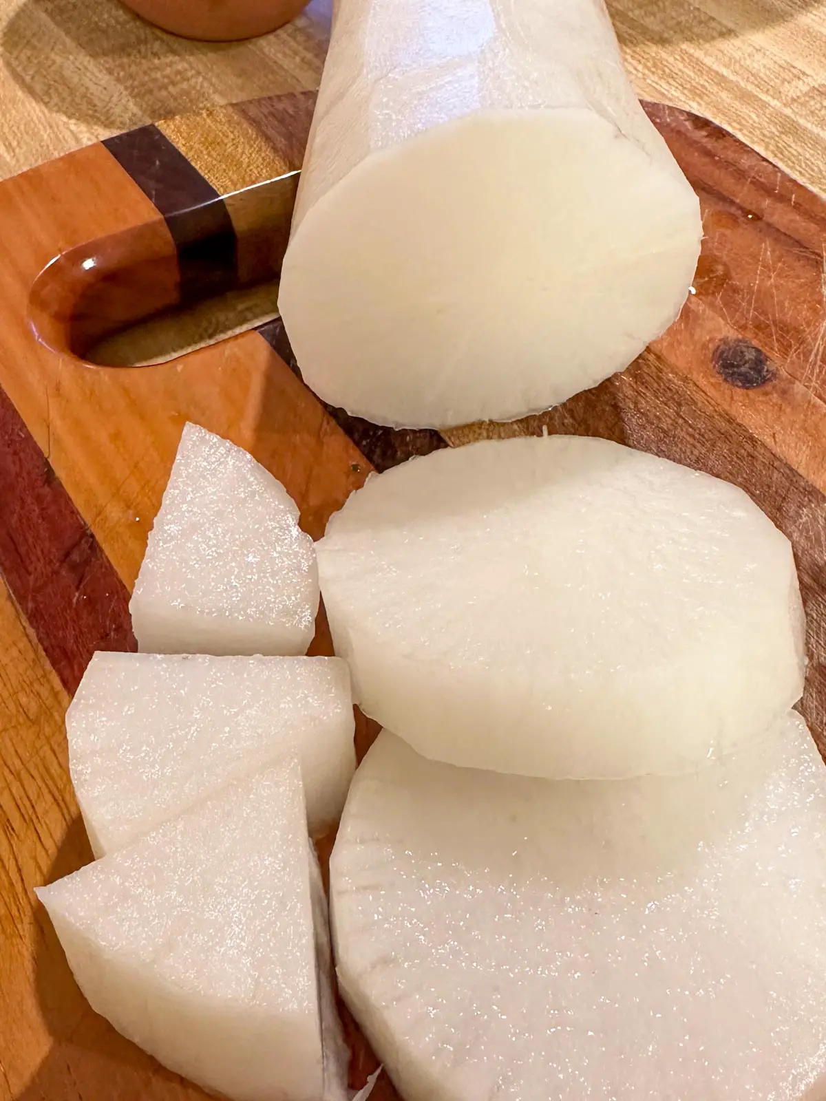 A peeled daikon radish which has been cut. There are small cubed pieces, 2 disc shaped pieces, and a tube shaped piece on top of a cutting board.