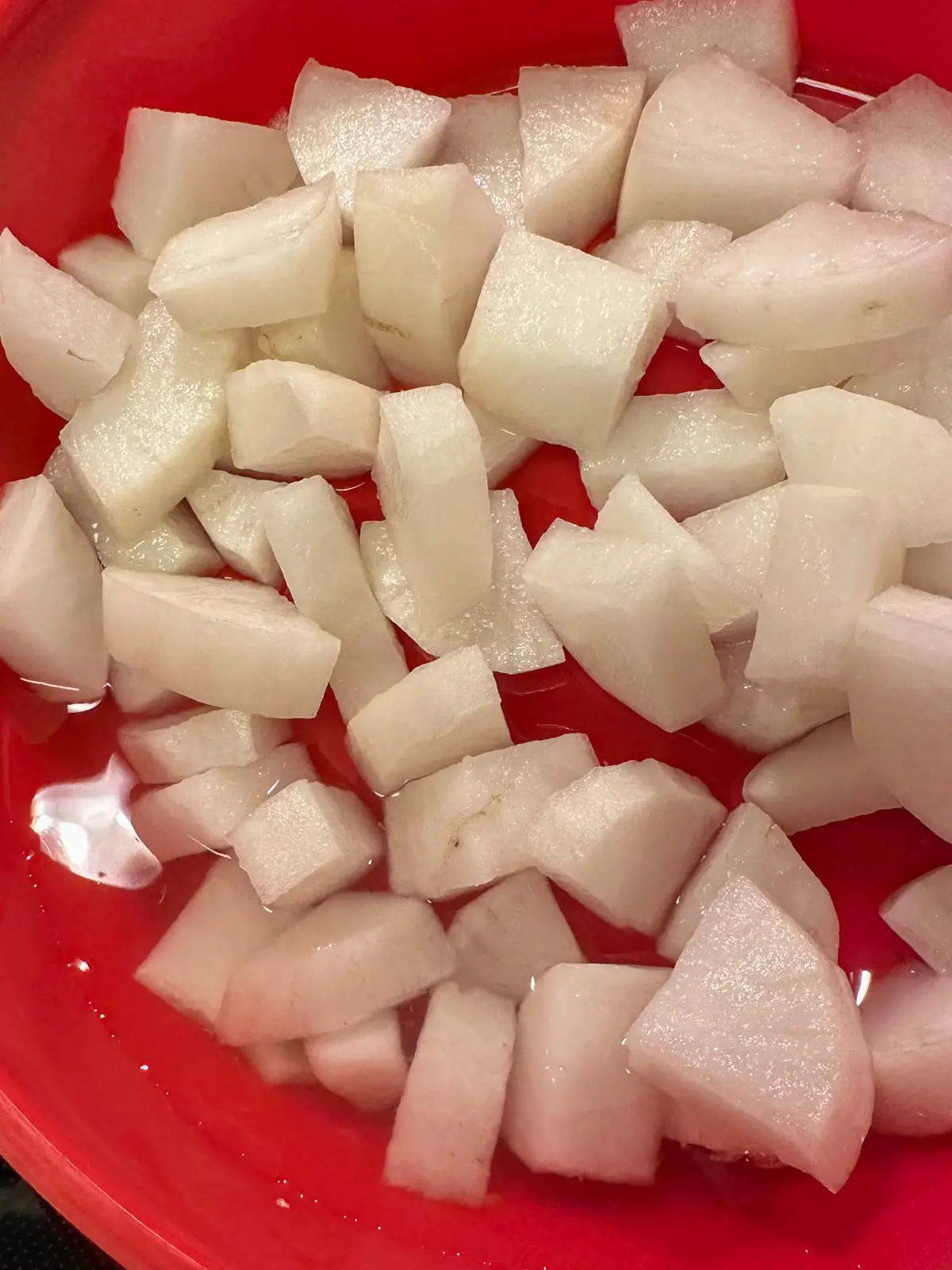 Cubed pieces of daikon radish with juices from the radish which have been released, in a red bowl.