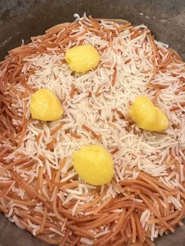 A saucepan containing cooked basmati rice and vermicelli topped with 4 dollops of ghee.