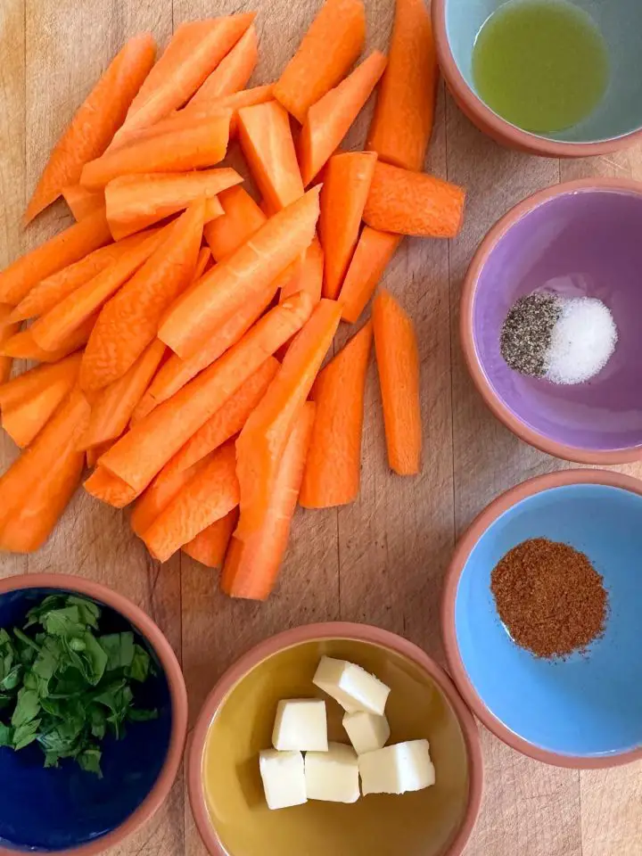 Sliced carrots and small bowls filled with olive oil, salt and pepper, Berbere spice, cubes of butter, and Italian parsley.