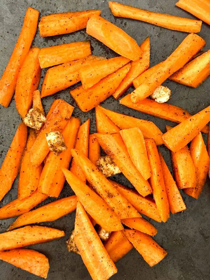 Sliced carrots seasoned with Berbere spice dotted with butter in a roasting pan.