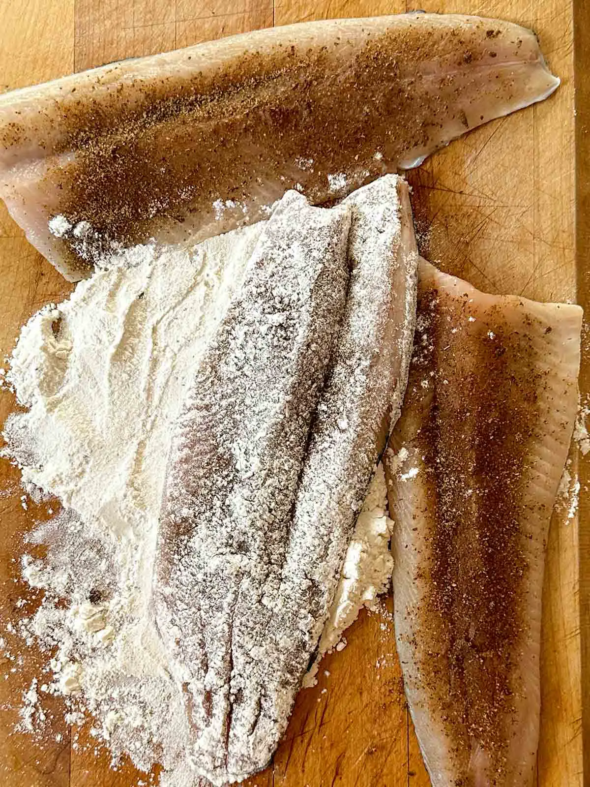 Seasoned rainbow trout fillets with one fillet coated with all purpose flour.