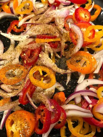 Sliced red onion, and colored bell peppers with seasonings sprinkled over the vegetables.