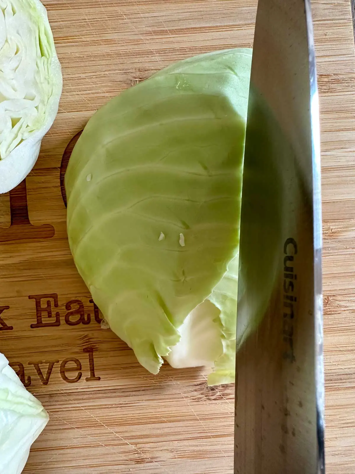 Green cabbage split into green and white parts on a wooden cutting board. This is a knife poised over one of the parts of the cabbage.