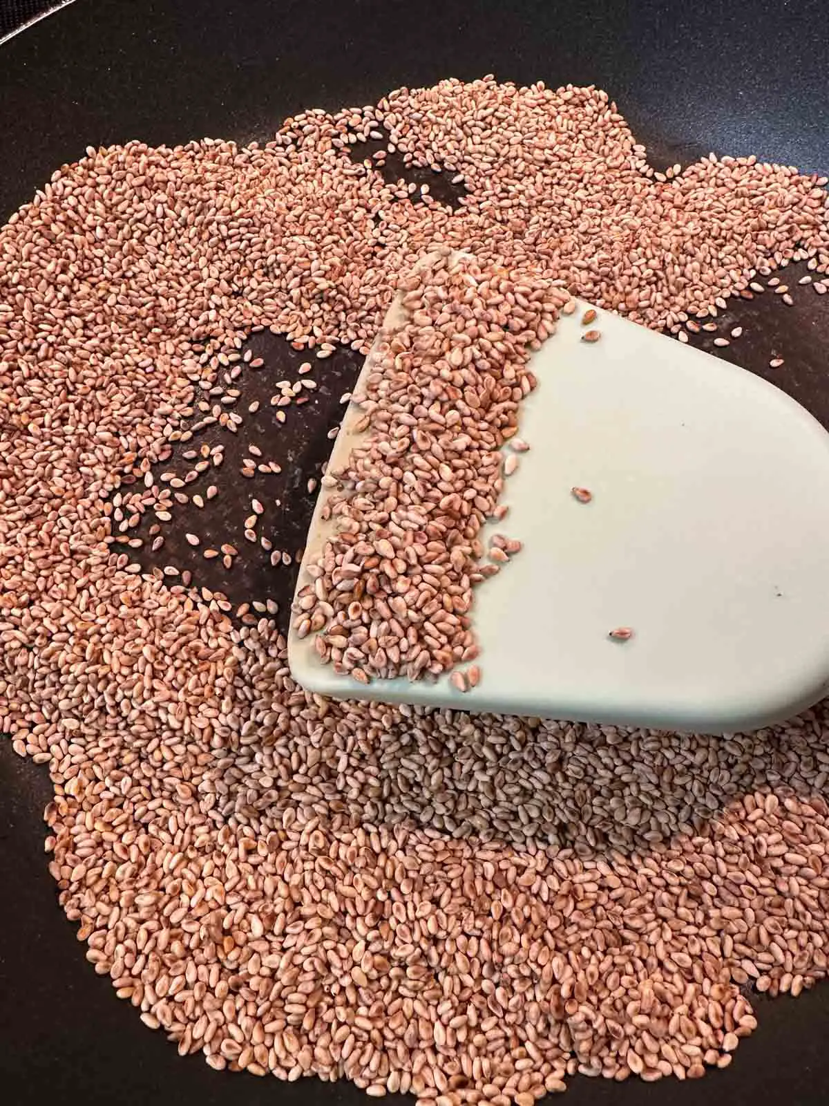 Toasted sesame seeds in a pan with a blue spatula holding some of the sesame seeds.