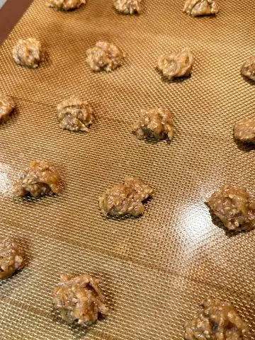 Dollops of uncooked benne wafer dough on a silicone baking mat.