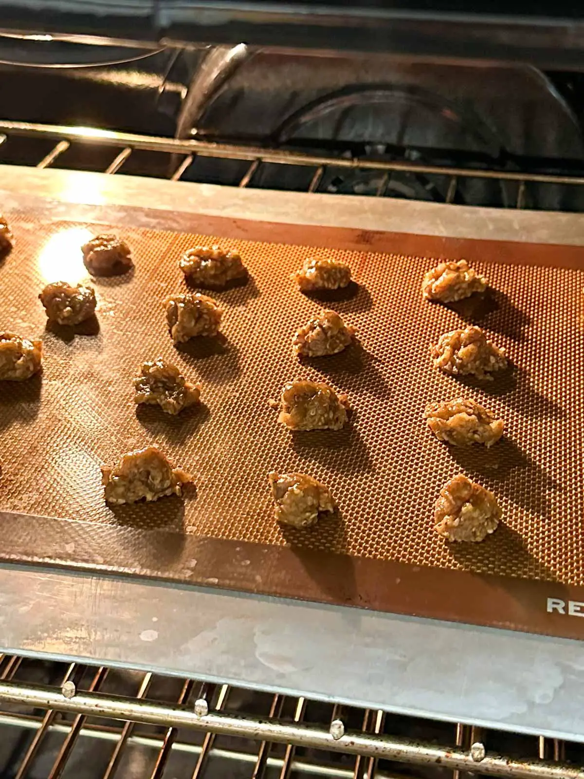 Benne wafers baking on a silicone baking mat on top of a baking tray in the oven.