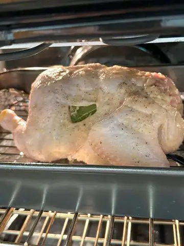 A roasting tray containing an uncooked whole chicken on a wire rack in the oven.