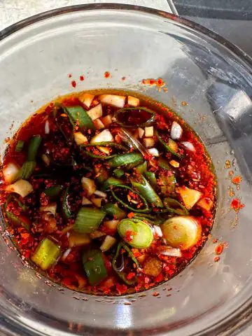A glass bowl filled with soy sauce, minced garlic and green onions and red chili flakes.