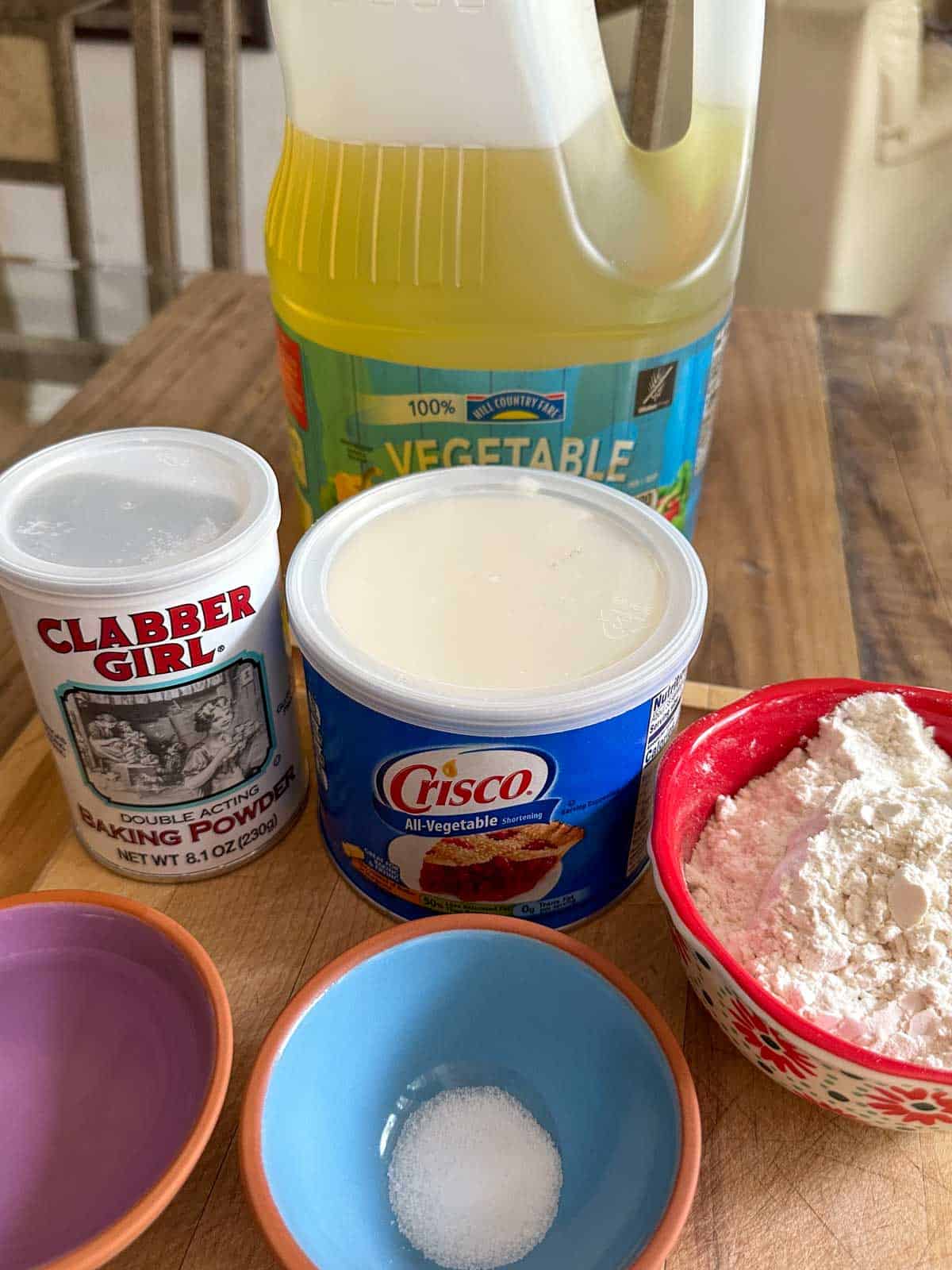 Vegetable oil container, baking powder container, Crisco vegetable shortening container, small red bowl with flour, and small bowls with water and salt.