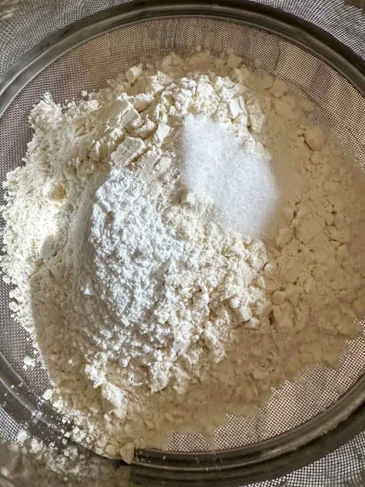 A glass mixing bowl containing flour, baking powder, and salt.