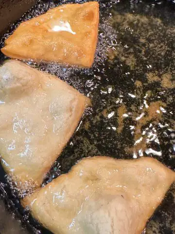 Belizean fry jacks frying in oil in a cast iron pan.