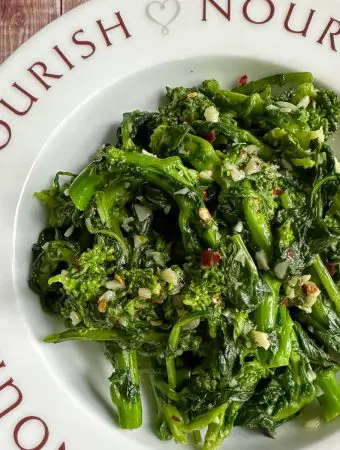 Sautéed Rapini with garlic and red chili flakes in a bowl that has the word "nourish" on it and pictures of hearts.