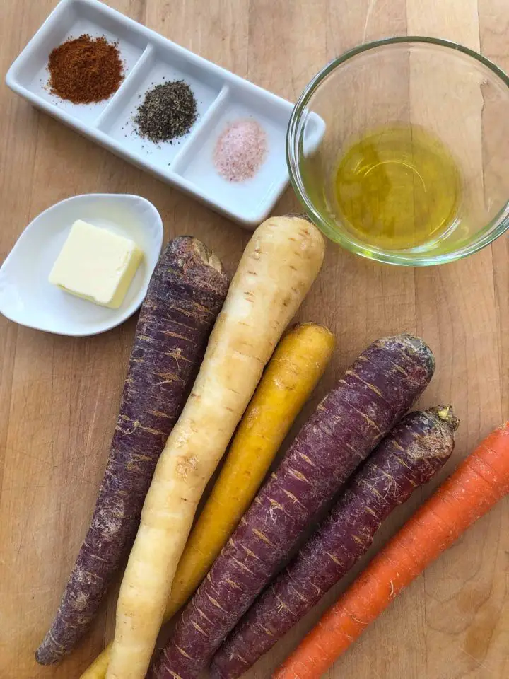 Whole multicolored carrots, a glass bowl with olive oil, a small dish with butter, and a dish with Berbere spice, pepper, and pink salt.