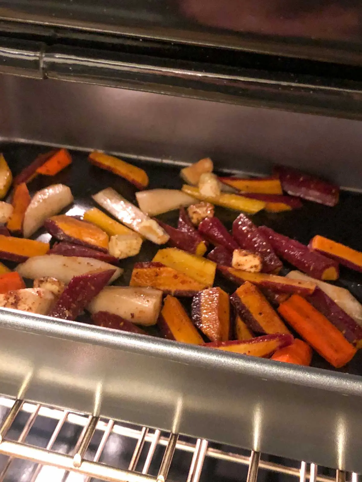 Slices of multicolored carrots with Berbere spice dotted with butter in a roasting pan in the oven.