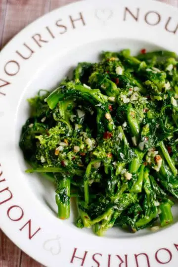Sautéed Rapini with garlic and red chili flakes in a bowl that has the word "nourish" on it and pictures of hearts.