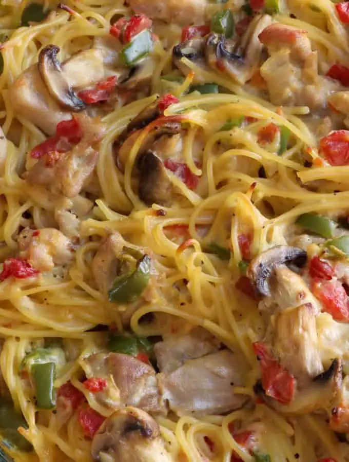 A glass casserole dish containing Texas Chicken Spaghetti which is spaghetti in a creamy sauce with tomatoes, mushrooms, chicken green chilies, and green bell peppers.