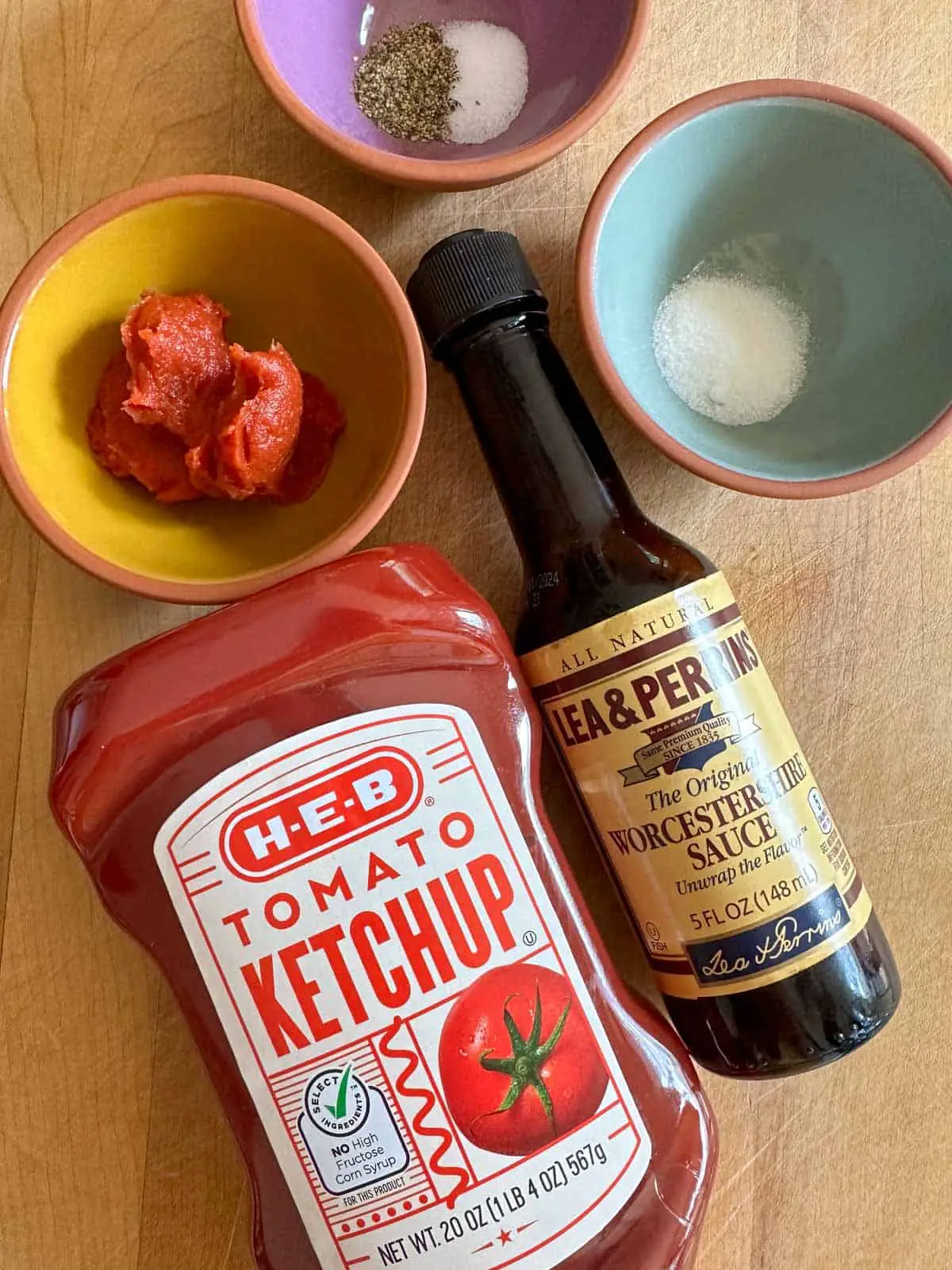 Bottle of ketchup, bottle of Worcestershire sauce, and bowls containing tomato paste, sugar, and salt and pepper.