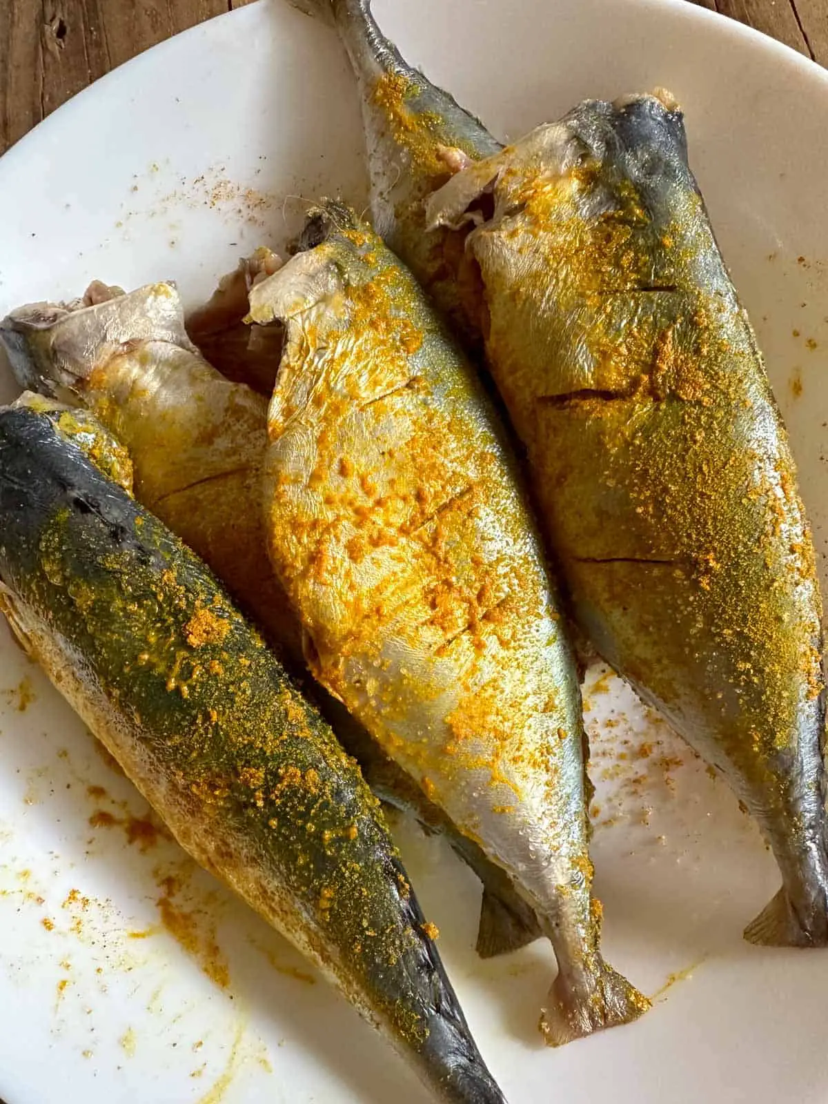 Uncooked mackerel coated with salt and turmeric in a white bowl.