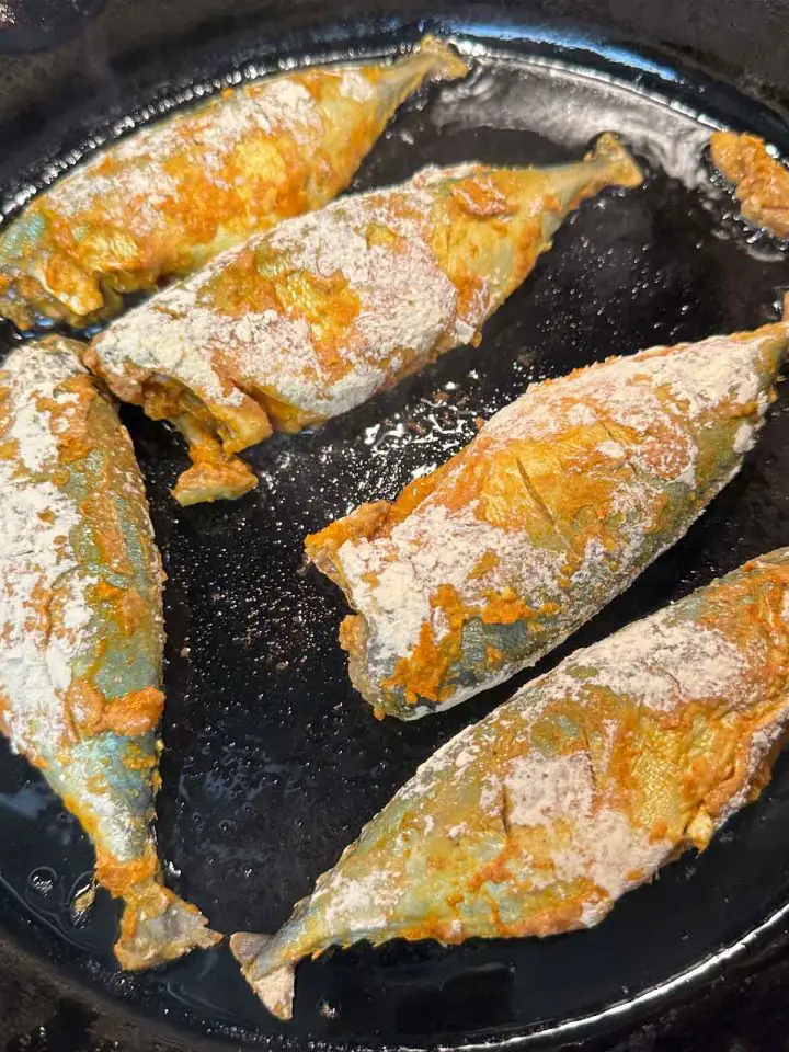 Mackerel coated with Indian spices and besan flour frying in oil in a cast iron pan.