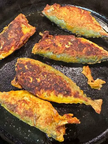 Mackerel which were coated in Indian spices being pan fried in a cast iron pan. They have turned brown and crispy.