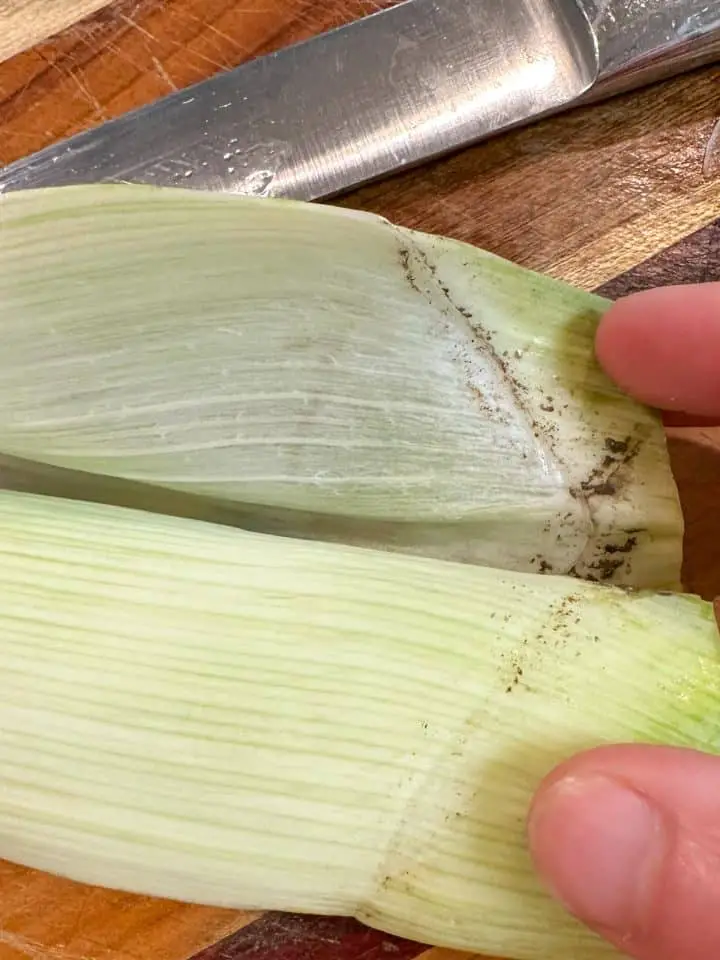 Leeks that have been peeled back to show grit that needs to be cleaned and a knife in the background.