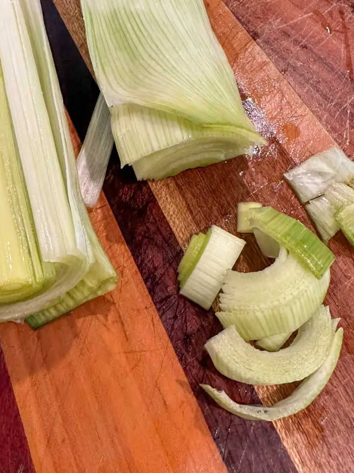 Leeks on a wooden cutting board. Some of the leeks have been sliced into half moon shapes.