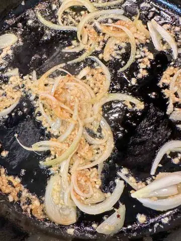 Sliced onion and minced garlic in melted butter and olive oil cooking in a cast iron pan.