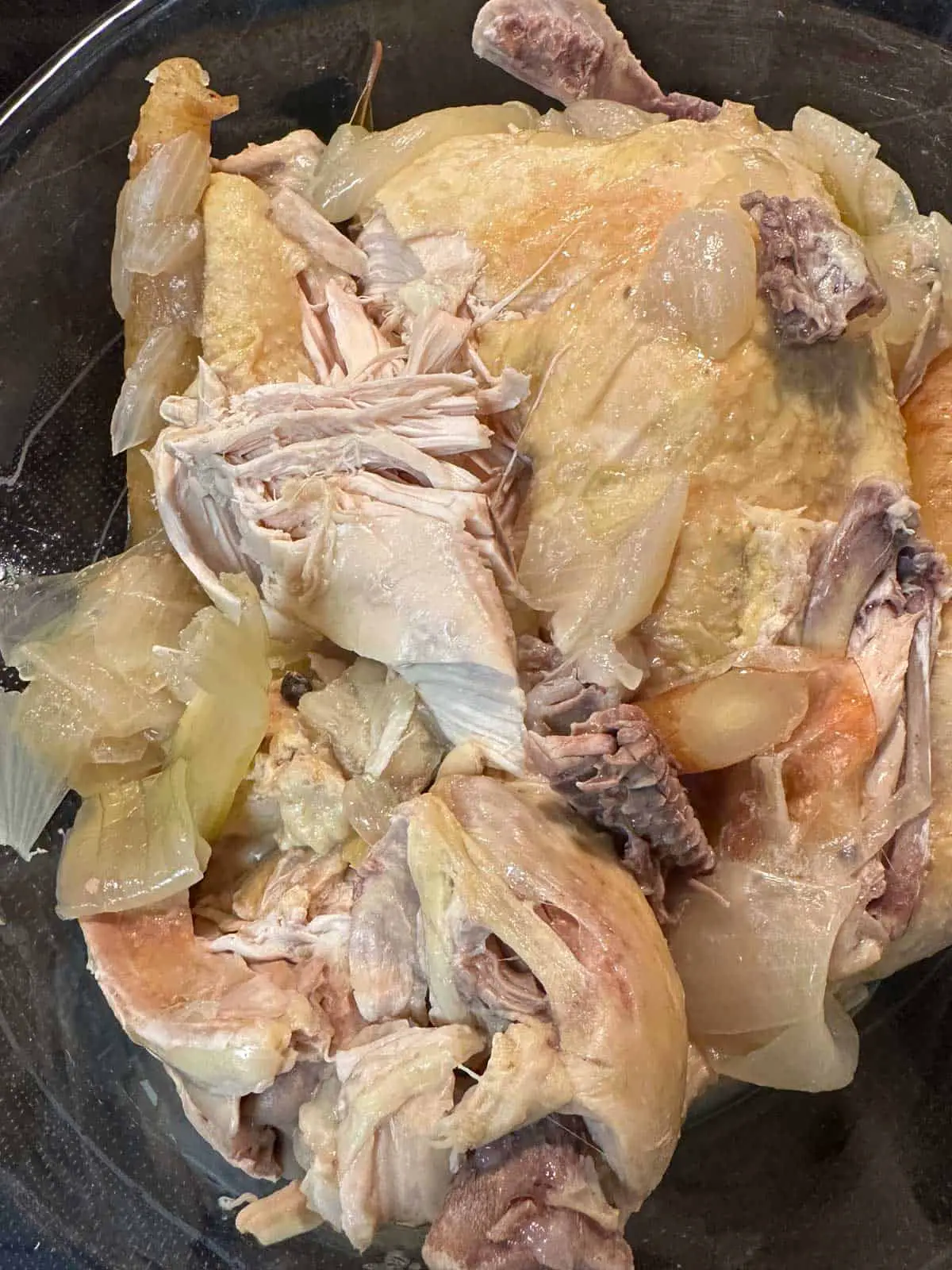 Cooked chicken which has been broken up so you can see some of the bones and the meat, and some cooked onions and carrots.