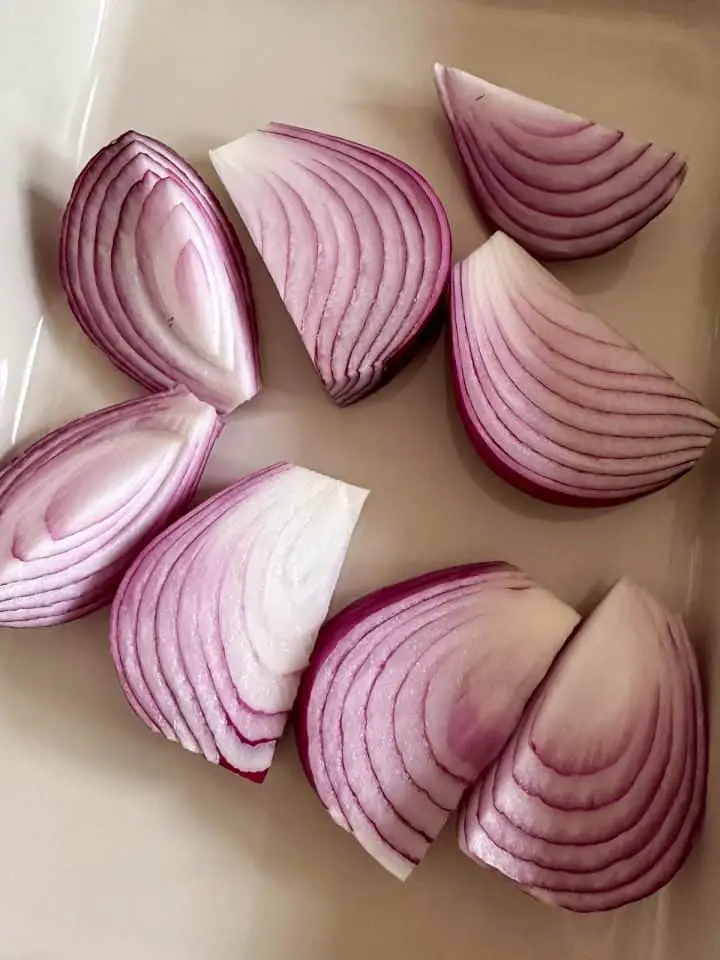 A casserole dish with 8 wedges of raw red onions.