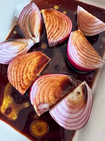 Red onion wedges and balsamic vinegar in a casserole dish.